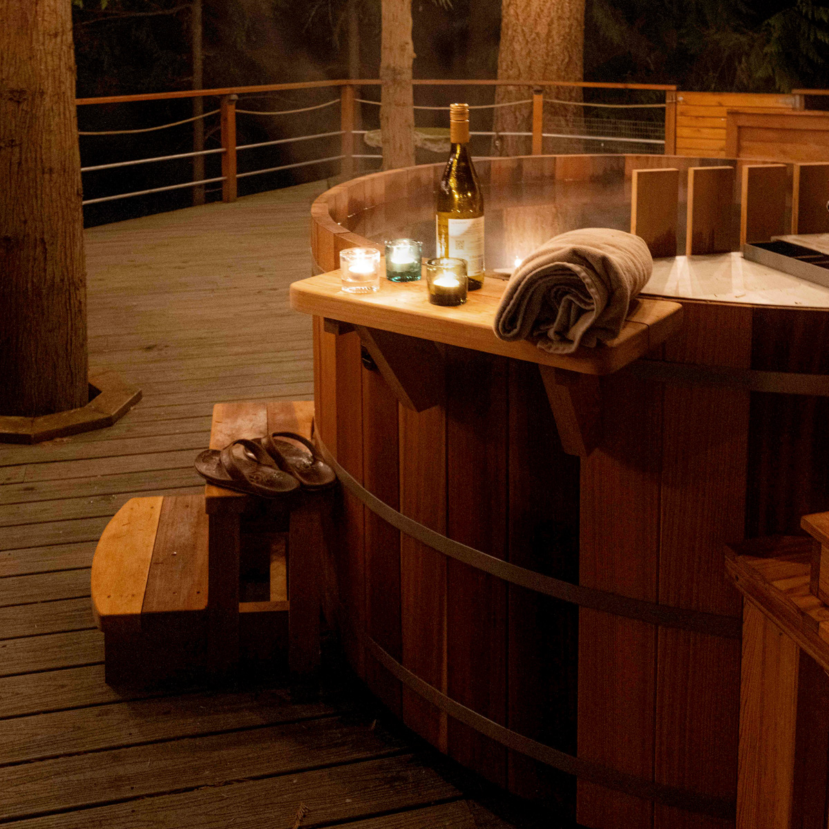 Steaming hot tub at night with candles and a bottle of wine