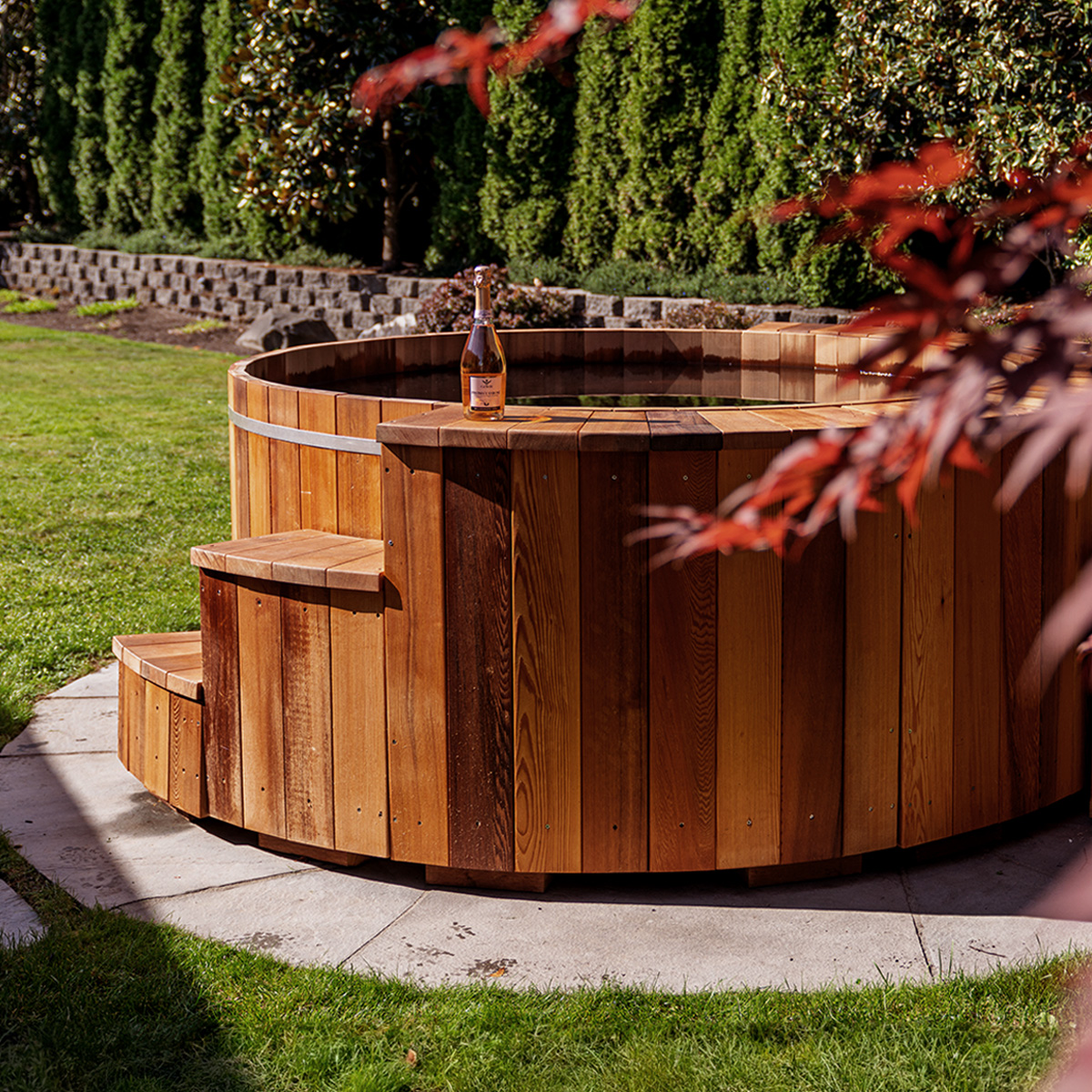 Cedar hot tub in a sunny back yard with a bottle of wine